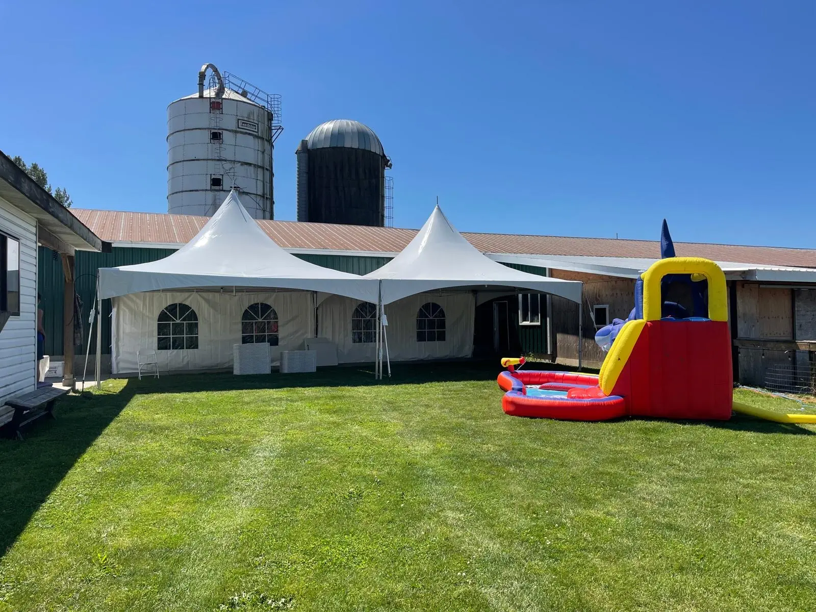 Two white high-peak tents installed beside a barn for a family event