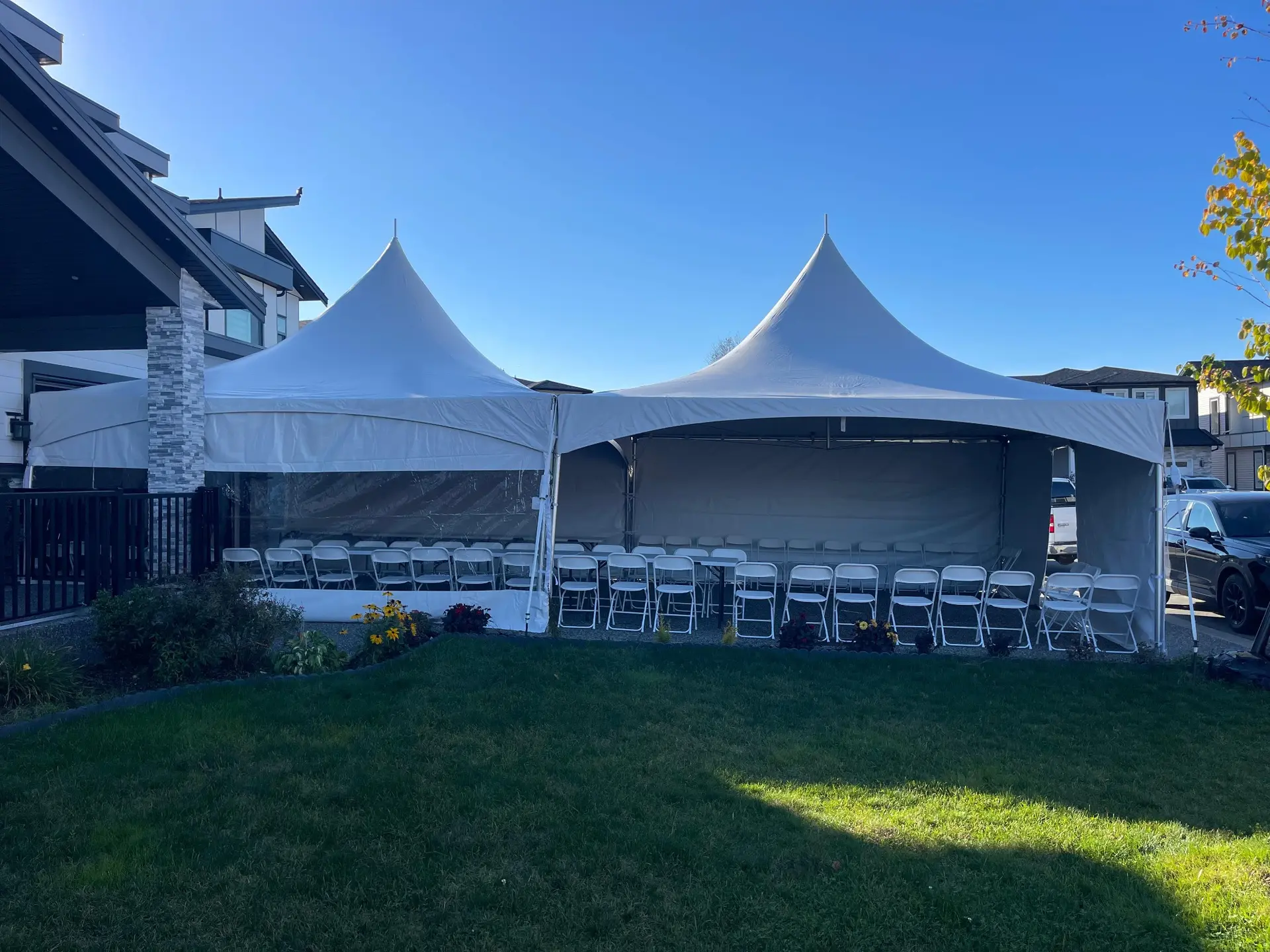 Two connected white high-peak tents with seating in a residential yard